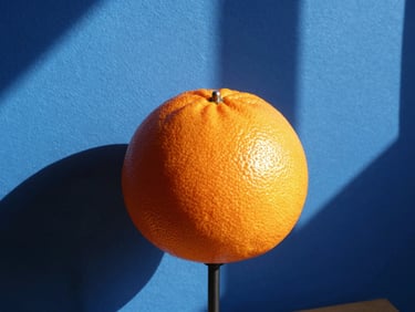 A close-up of a modern sculptural tangerine table lamp casting sharp geometric shadows on a cobalt blue wall, direct sunlight, 35mm lens