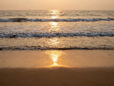 A quiet sandy beach in Puri at sunrise, gentle waves, warm golden light reflecting on the water.