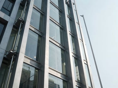 Clean architectural shot of a finished glass and steel elevator shaft in a modern Indian building, bright daylight, heavy steel guide rails visible.