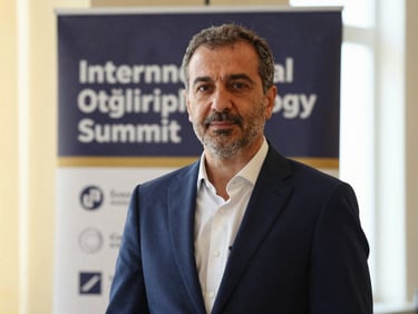 Medium close-up portrait of Dr. Öğretmenoğlu in a tailored navy suit, standing confidently in front of an international ophthalmology summit banner, warm lighting.