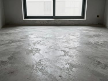 After: same residential floor now finished in polished concrete, daylight from the same window revealing uniform sheen and smooth aggregate surface, no furniture