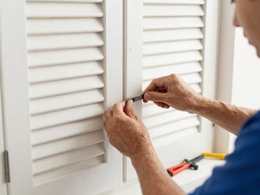 Gros plan sur une manivelle de volet roulant cassée, les mains d'un artisan prêt à la remplacer, outils à portée de main, ambiance de réparation.