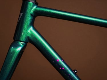 Macro photography of a custom bicycle frame paint finish, deep metallic green gradient with electric magenta flecks catching dramatic studio light, 35mm