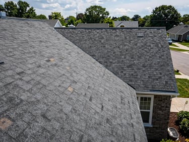 Wide shot of a completed residential roof replacement, new shingles running clean to ridge cap, viewed from street level, natural Rochester daylight, no people