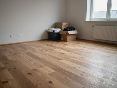 Close documentary shot of a cleared bedroom floor in a Breton apartment, bare floorboards visible, a few personal items sorted into boxes near the wall, flat overcast light from a window, no people