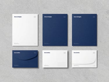 Strict orthographic projection of a modern brand identity system, slate blue and white stationery arranged in perfect alignment on a light gray concrete surface, cool diffused daylight.
