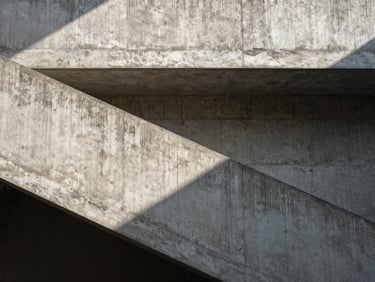 Flat-on architectural detail of a brutalist concrete staircase, sharp shadows, natural overhead skylight illuminating raw texture.