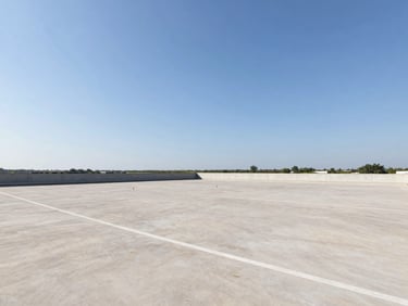 Wide-angle architectural shot of an open, flat land parcel with clear boundary markers under a bright midday sky, natural colors, sharp focus.