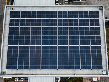 Aerial view looking straight down at a large commercial rooftop solar installation, panel rows in precise geometric formation across the full width, slight overcast diffusing shadows, scale apparent from HVAC units visible at lower edge of frame