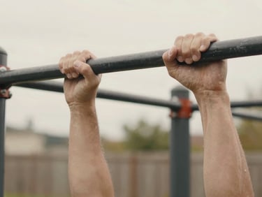 Candid close-up of chalked hands gripping a black steel pull-up bar in a backyard, natural overcast daylight, 35mm.