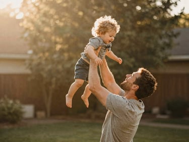 Candid shot of a father lifting his toddler in the air in a sun-drenched backyard, warm golden light, shallow depth of field