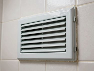 Small UPVC louvered bathroom ventilator frame installed in a tiled wall, close-up showing the adjustable slat mechanism and the frame-to-wall mortar joint, even indoor light