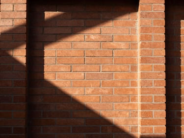 Tight graphic architectural close-up of a terracotta brick wall with natural high-contrast sunlight casting deep geometric shadows, 35mm