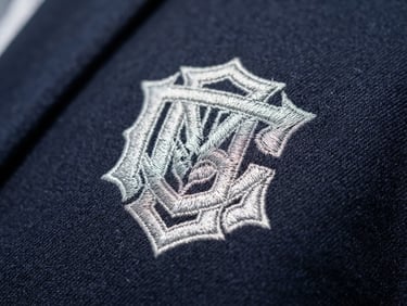 Close-up of high-precision embroidery on a navy blue corporate jacket, sharp focus on silver thread stitches, professional lighting, 35mm