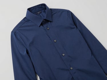 Plano medio de una camisa corporativa azul marino bien estructurada expuesta sobre un fondo gris neutro, enfoque nítido en las costuras, luz de estudio, 35mm.