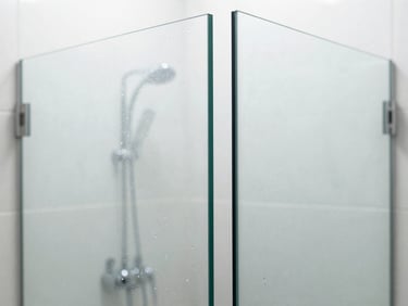 Crisp architectural macro shot of a frameless glass shower partition with flawless diamond-polished edges, clean water droplets sliding off, diffused natural daylight, 35mm