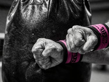 Close-up of tightly wrapped hands punching a heavy leather bag, sweat spray, high-contrast black and white photography