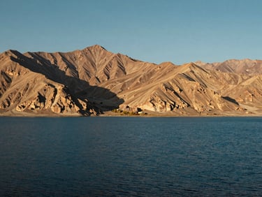 Expansive environmental shot of Pangong Lake in Ladakh, deep blue water contrasting with rugged barren mountains under a clear sky