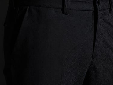 Close-up of heavy-gauge black textile weave on tailored trousers, sharp focus on the architectural seam line, low-key dramatic side-lighting with deep obsidian tones.