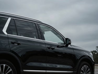 Low-angle profile of a black armored executive SUV, polished surface reflecting overcast DC sky, low-key dramatic lighting, cool desaturated tones.