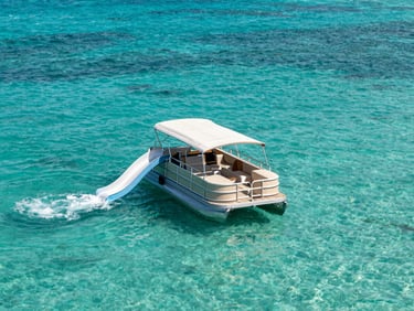 Wide-angle view of a double-decker pontoon boat with a built-in water slide anchored in turquoise Florida shallows, bright midday sun, clear water