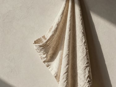 Finished linen garments draped elegantly on a textured plaster wall, natural shadows