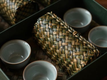 Macro detail of hand-woven bamboo basketry and ceramic tea cups within a gift set, soft, warm lighting highlighting textures, dark moody editorial photography.