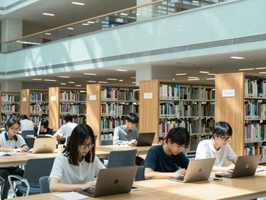 Modern university campus library, students studying on laptops, natural light, wide shot