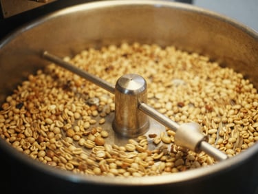 A close-up of coffee roasting drum window showing glowing yellow and brown beans spinning inside, soft motion blur, warm golden light, 35mm lens.