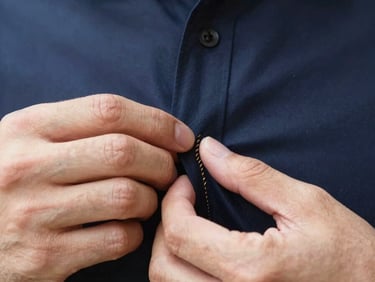 Close-up of hands meticulously tailoring a shirt, focusing on stitch detail and fabric texture, natural light, sharp editorial style.
