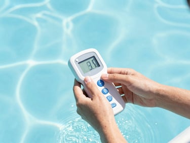 Hands adjusting a digital water tester over crystal-clear pool water, bright high-key sunlight, 35mm