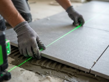 Macro view of a laser level casting a sharp green line across grey porcelain tiles, hands in protective gloves aligning a tile, high contrast, clean architectural photography, 35mm lens