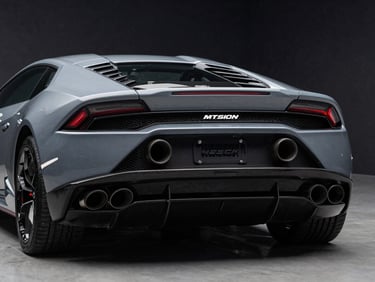 Rear angle of a Grigio Lynx Lamborghini Huracán Evo showing the dual exhaust pipes and carbon fiber diffuser, moody low-key lighting.