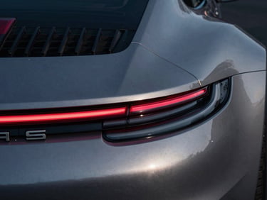 Dramatic close-up of a modern Porsche 911 tail-light geometry at night, sharp metallic reflections, low-key lighting
