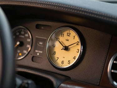 Macro shot of a hand-stitched leather dashboard and analog clock in a luxury vehicle, warm golden instrument lighting, dark premium interior.