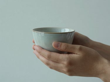 Close-up of hands holding a warm ceramic cup, soft diffused daylight, gentle shadows, minimalist setting, 35mm