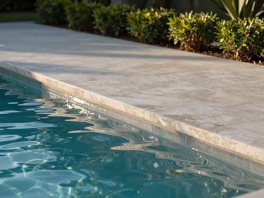 Close detail of the pool edge at Royal Pool Villa — smooth concrete coping, water surface reflecting afternoon light, garden border with low shrubs behind, no people, purely the finished surface in natural daylight