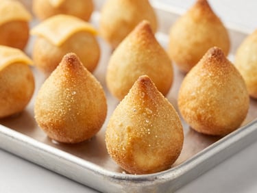 Macro shot of perfectly golden coxinhas and cheese breads on a clean steel industrial baking tray, warm lighting, high detail
