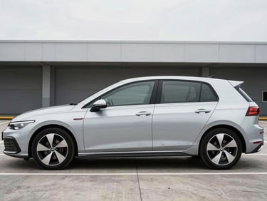 Wide three-quarter front profile of a silver hatchback parked in a clean modern parking facility, bright overcast daylight from above, no people, minimal background