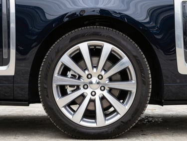 Close-up of the polished chrome wheel and side panel of a pristine executive black SUV, reflections visible, crisp daylight, 50mm lens.