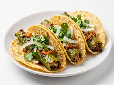 Three street tacos with grilled green nopales, white onions, and green cilantro on a white plate under soft daylight.