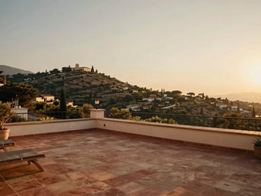 Cozy boutique hotel terrace overlooking a Mediterranean hillside at golden hour, warm terracotta tiles, soft natural light, cinematic wide-angle lens, warm editorial travel photography