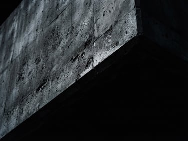 Macro detail of dark architectural concrete edge cutting diagonally, sharp chiaroscuro light, deep black shadows, cool silver tones, 35mm