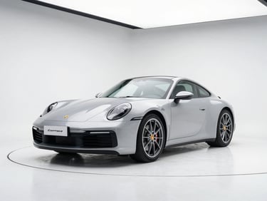 Three-quarter front angle of a silver 2021 Porsche 911 Carrera in a sleek white studio backdrop with overhead softbox lighting, 50mm lens
