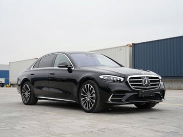 Three-quarter front angle of a metallic black 2022 Mercedes-Benz S580 parked on a clean shipping dock, bright overcast sky, 50mm lens