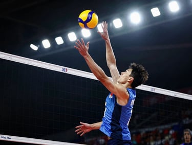 Tight action crop of a volleyball player spiking the ball over a net, high-contrast dramatic lighting, sharp stadium floodlights, cool tones.