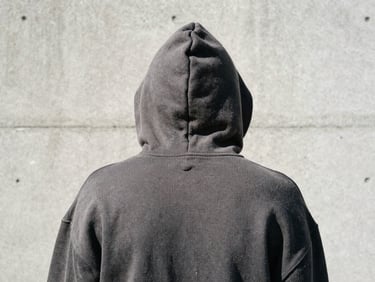 Close-up of a dark gray oversized hoodie hood, heavy texture, worn by a skater from behind, raw concrete background