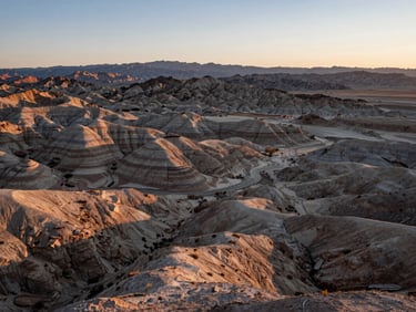 Wide panoramic view of the rugged Utah desert landscape at dawn, soft morning light illuminating textured earth and distant mountains
