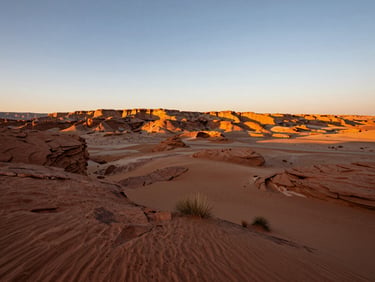 Wide panoramic Utah desert landscape at golden hour, low horizon, sweeping sand and rustic rock formations with deep terracotta tones.