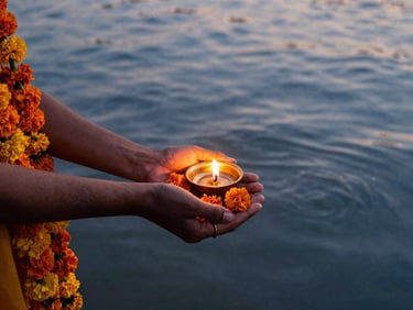 Close-up of hands gently offering orange marigold garlands to the sacred Yamuna river, soft water ripples, golden oil lamp glow, 35mm